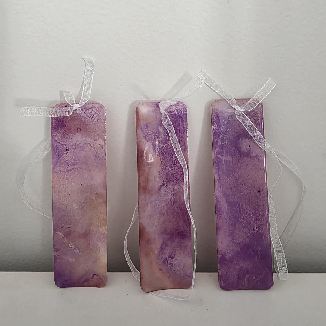 Three handmade alcohol ink bookmarks in vibrant purple and magenta tones with white ribbons