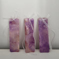 Three handmade alcohol ink bookmarks in vibrant purple and magenta tones with white ribbons