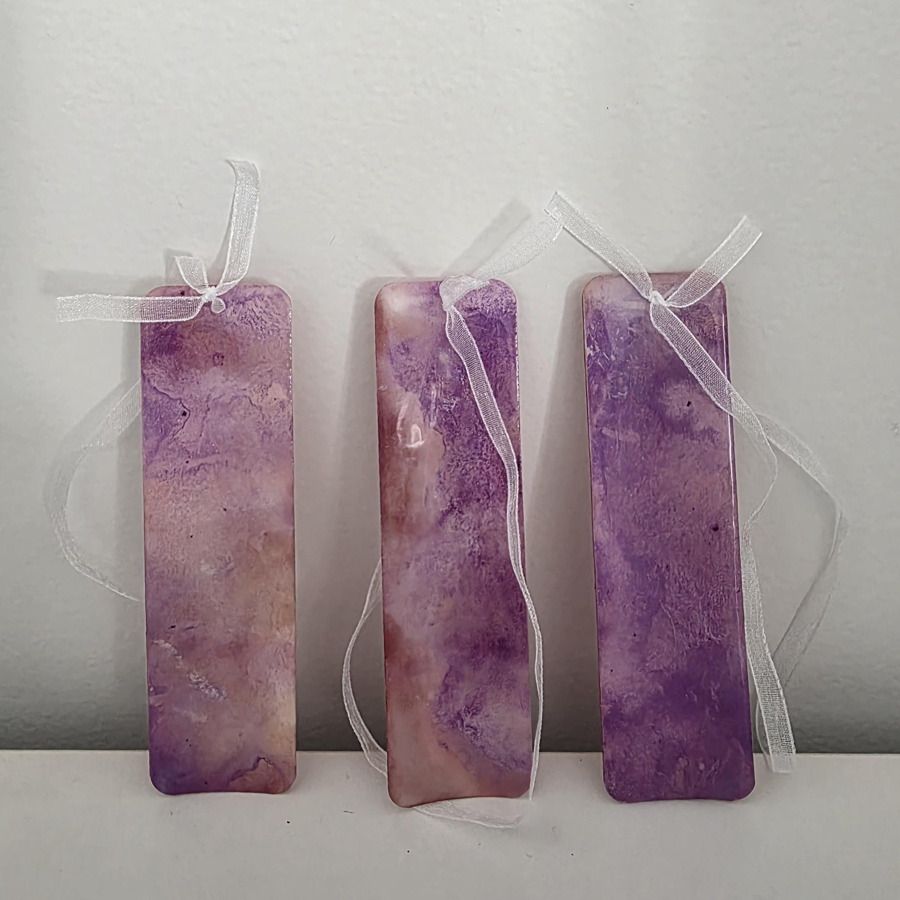 Three handmade alcohol ink bookmarks in vibrant purple and magenta tones with white ribbons