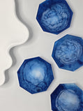 Top-down view of four blue resin and white eco-casting powder coasters showing abstract marble patterns.