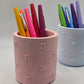 Pink cylindrical holder with colorful pens on a light gray background