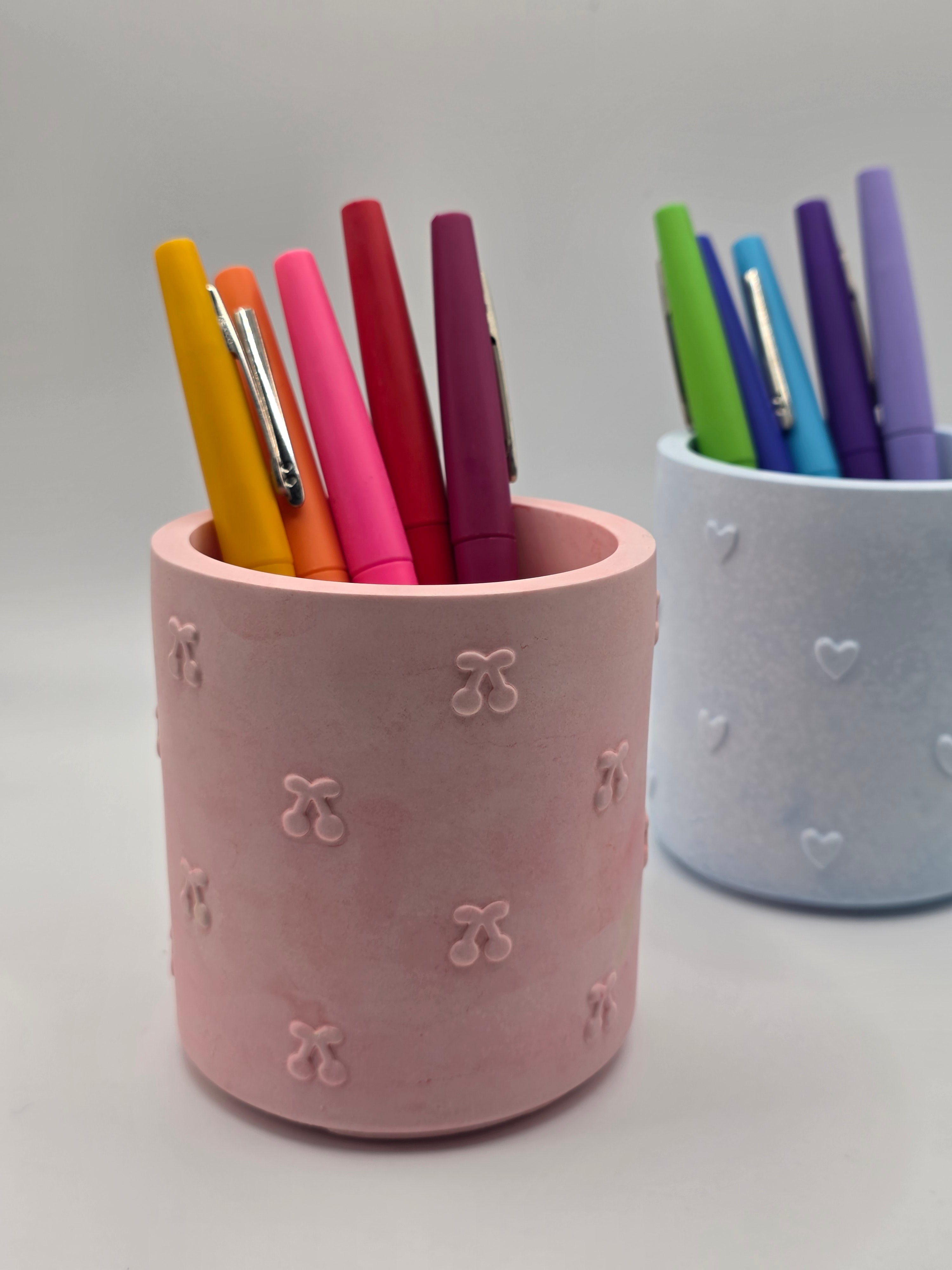 Pink cylindrical holder with colorful pens on a light gray background