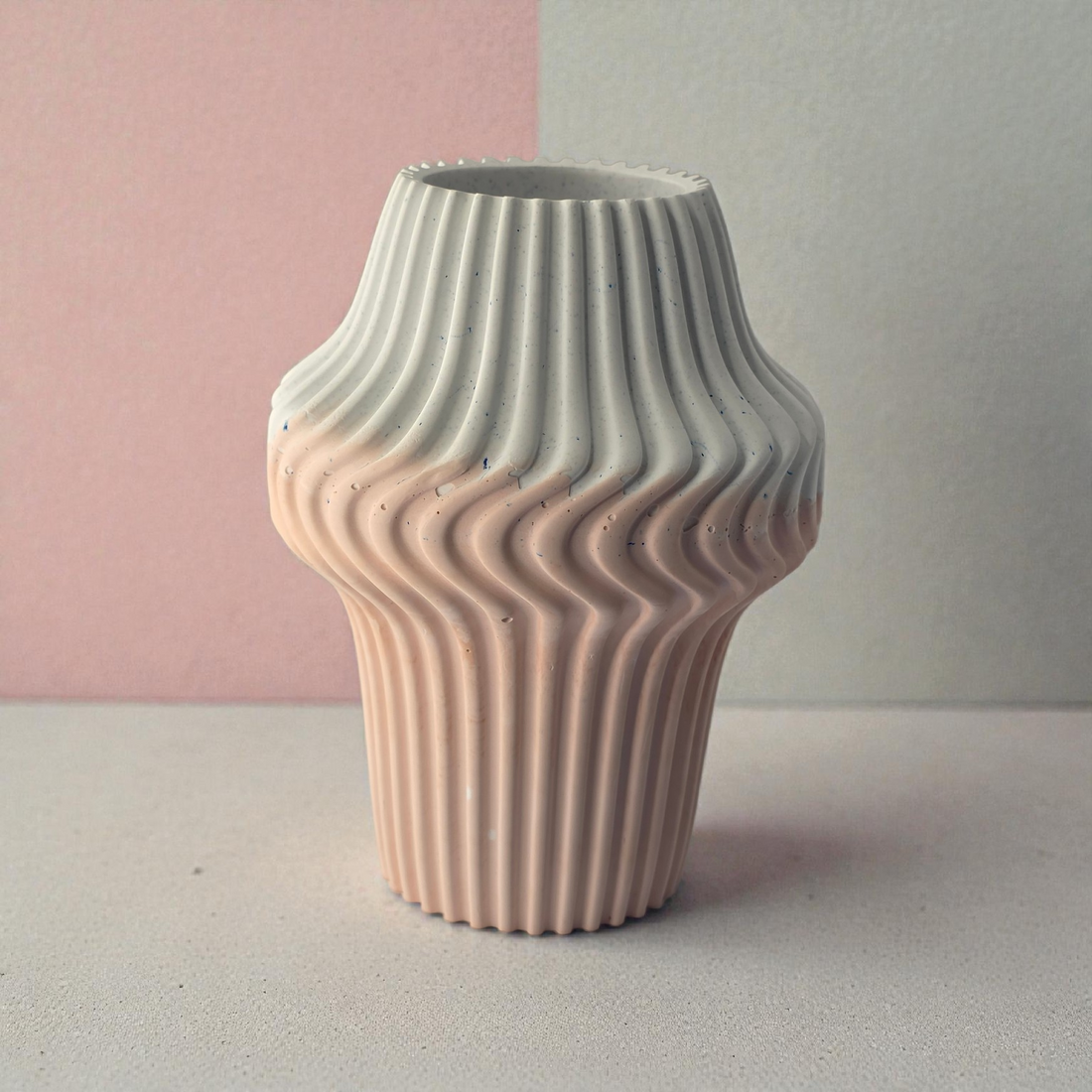 Front view of a modern ribbed vase with a soft pink to white ombre gradient, set against a two-tone pink and grey background.
