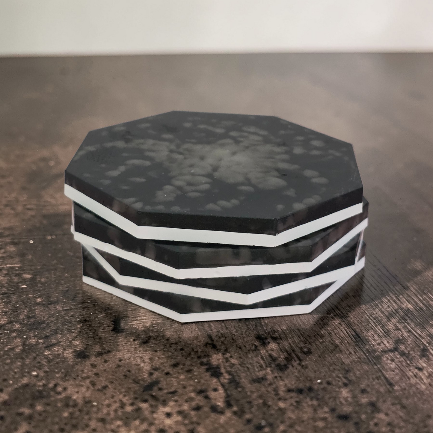 Stack of black and white Tasmanian made octagonal drink coasters on dark wood-look surface.