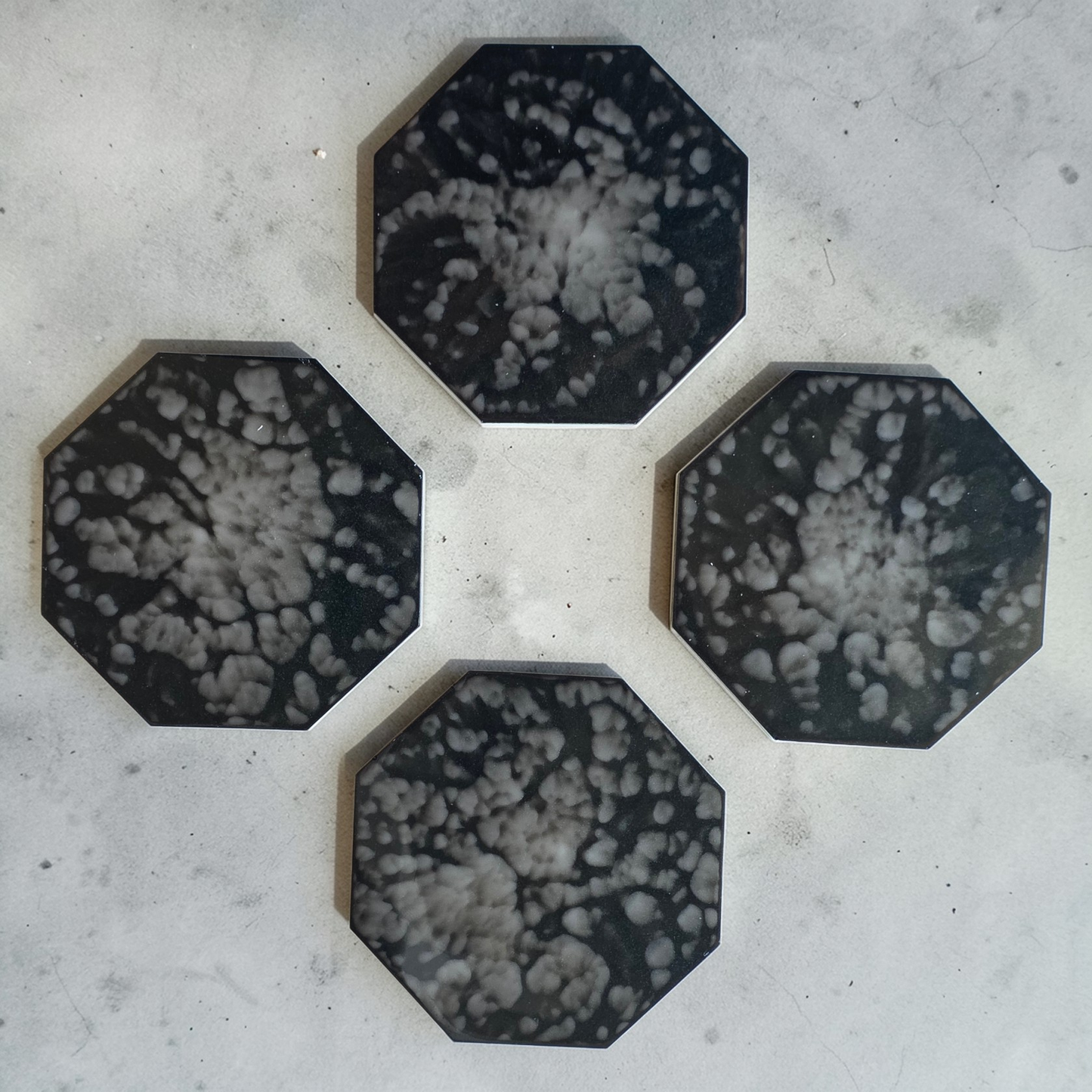 Four hexagonal drink coasters with a black and white pattern on a concrete surface