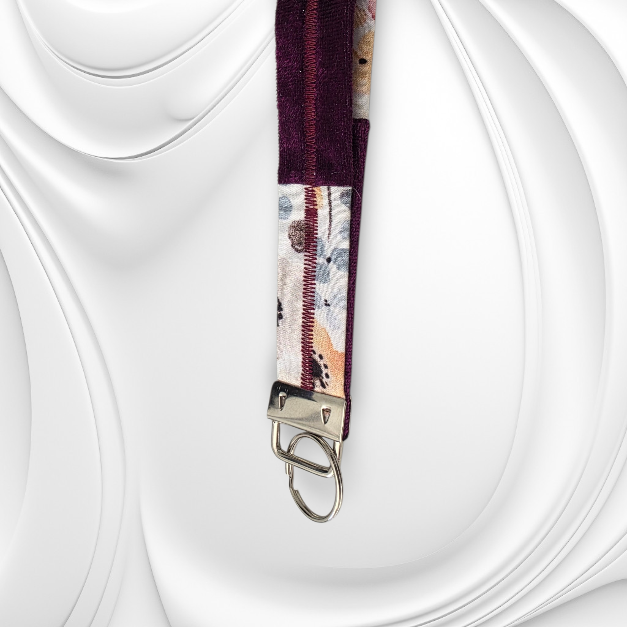 Close-up detail of a plum purple velvet and floral patterned fabric wristlet with silver hardware and reinforced stitching.