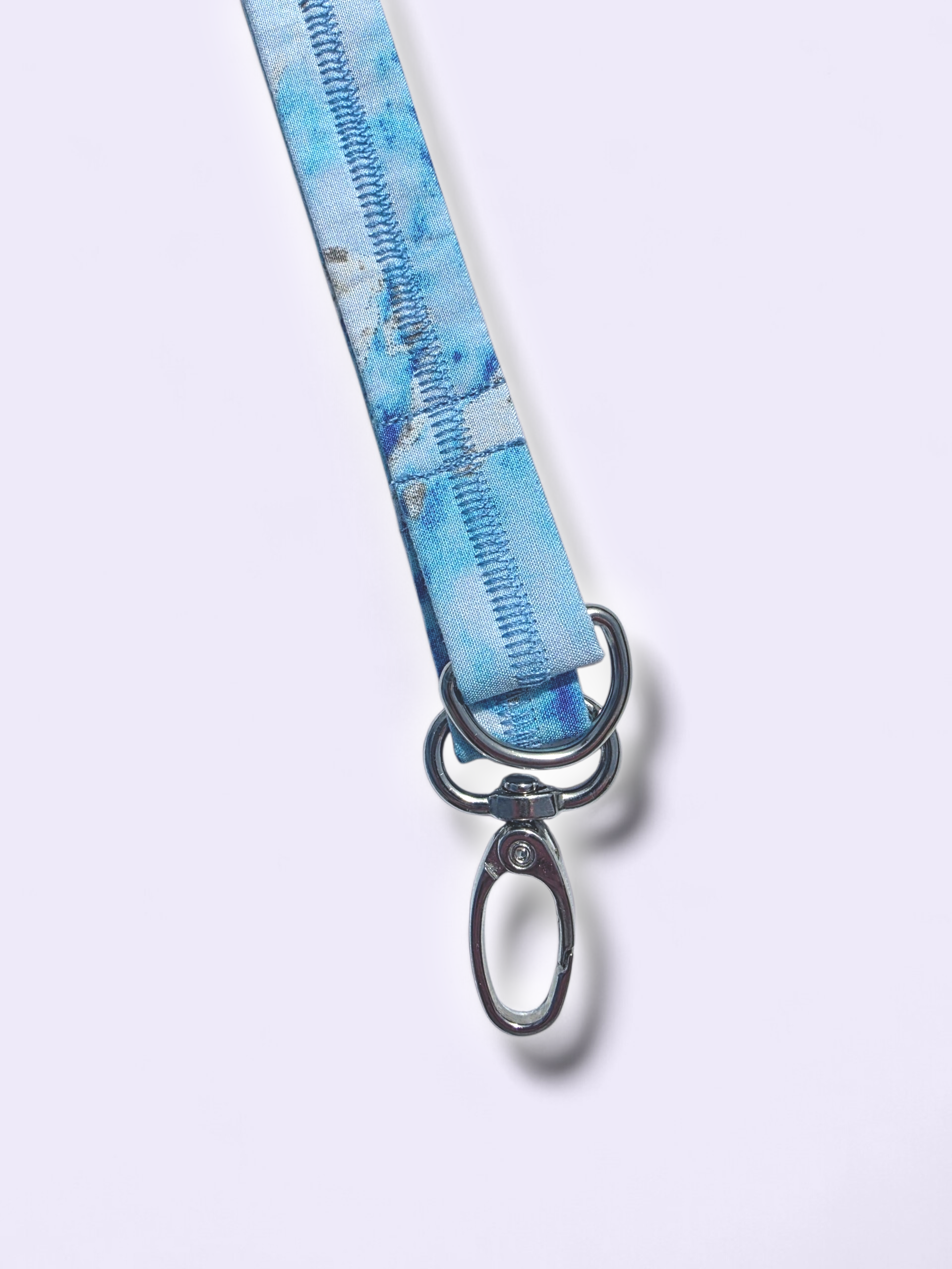 Close-up of silver swivel hook and D-ring hardware attached to a light blue marble fabric lanyard with reinforced stitching.