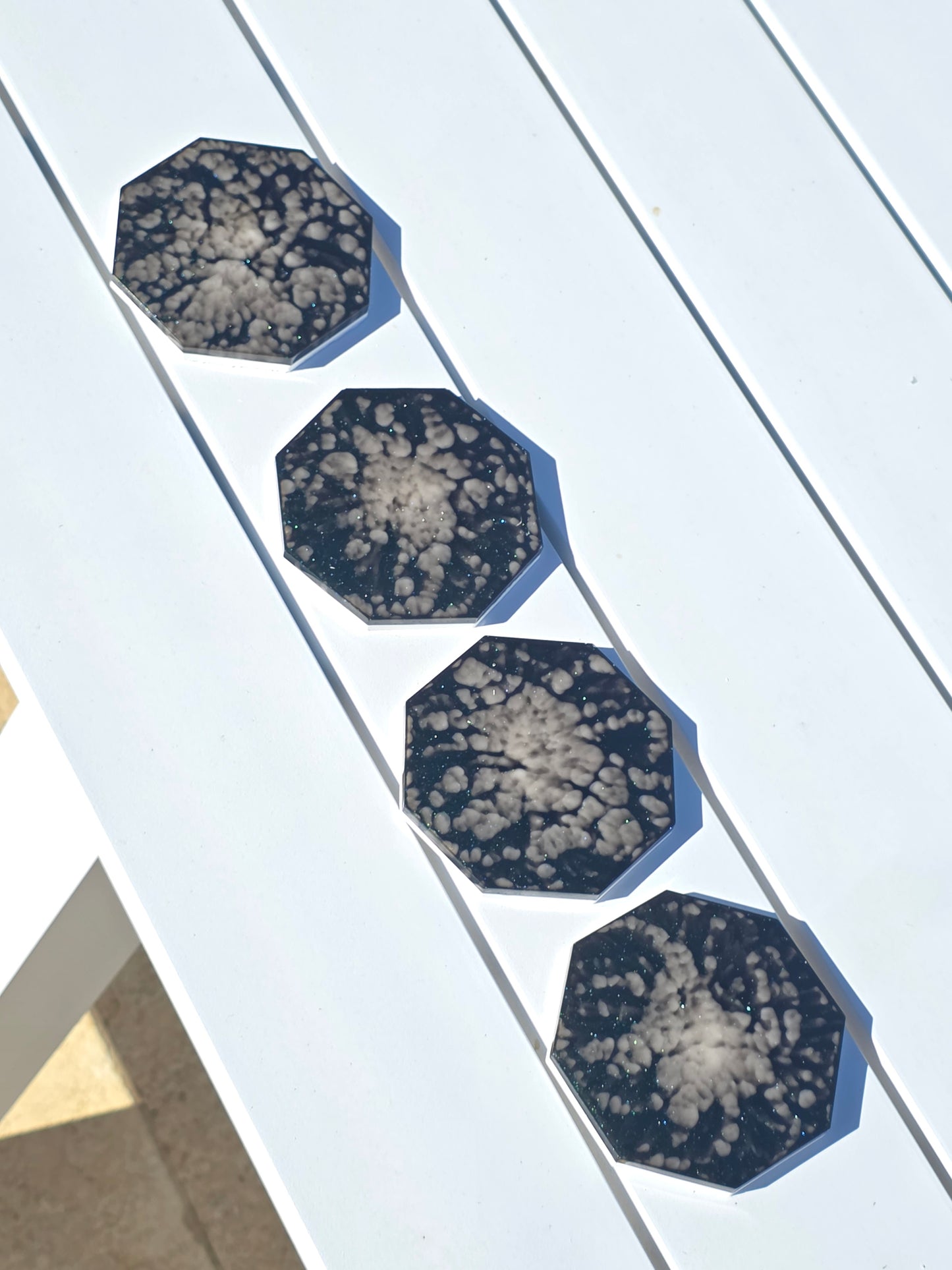 Four geometric coasters sparkling in the sun on an outdoor dining table.