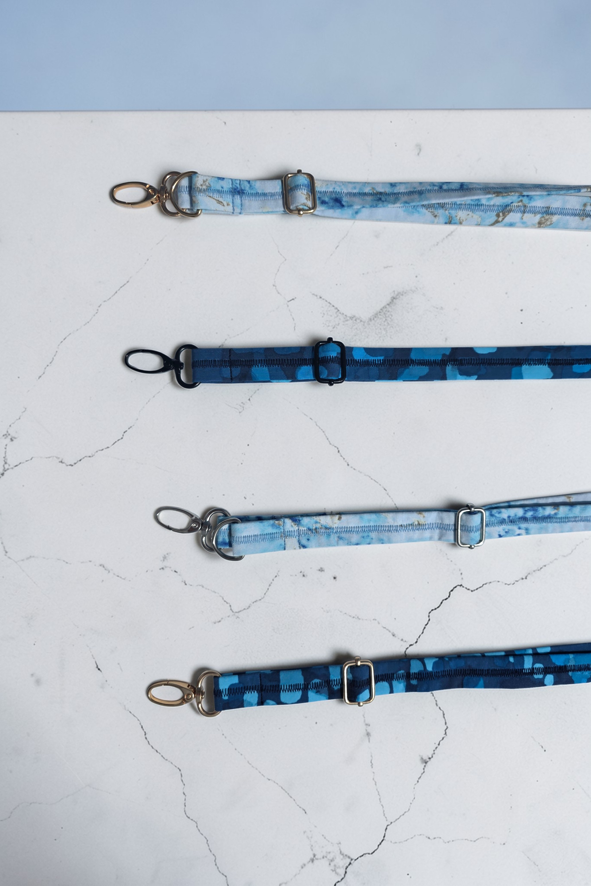 Comparison of gold, silver, and black metal lobster clasps and adjustment slides on various blue fabric straps.