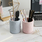 A pair of matte stone pen cups in pastel blue and pink with embossed heart patterns on a white marble desk next to a laptop