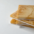 A stack of square honey-colored coasters tied with a rustic twine bow on a wooden coffee table next to a glass of water.
