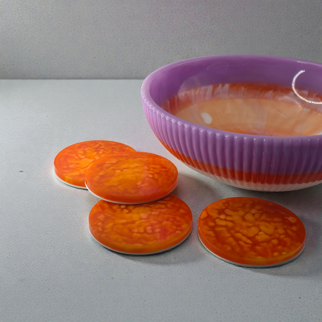 Orange marbled coasters in front of a purple bowl on a gray surface