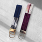 Two fabric keychains side-by-side: one navy and white with gold hardware, and one purple and floral with silver hardware.