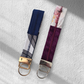 Two fabric keychains side-by-side: one navy and white with gold hardware, and one purple and floral with silver hardware.